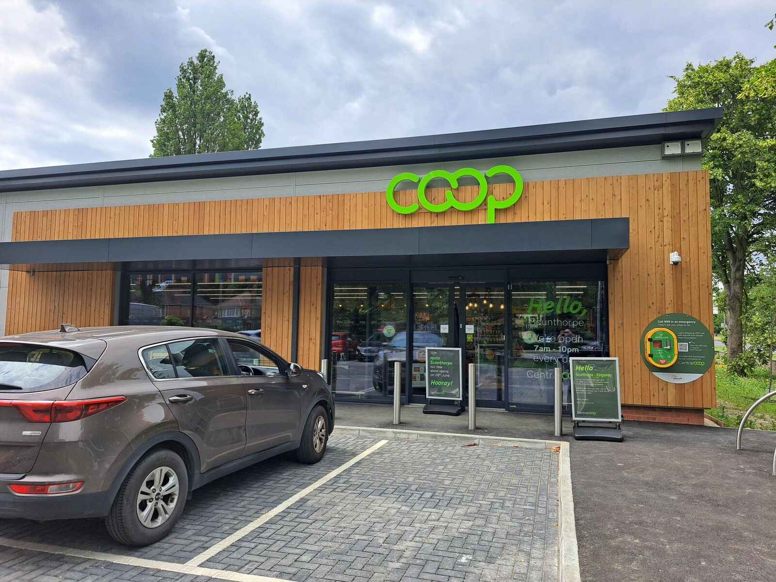 A gray car parked in front of a Coop store with wooden exterior and green signage.
