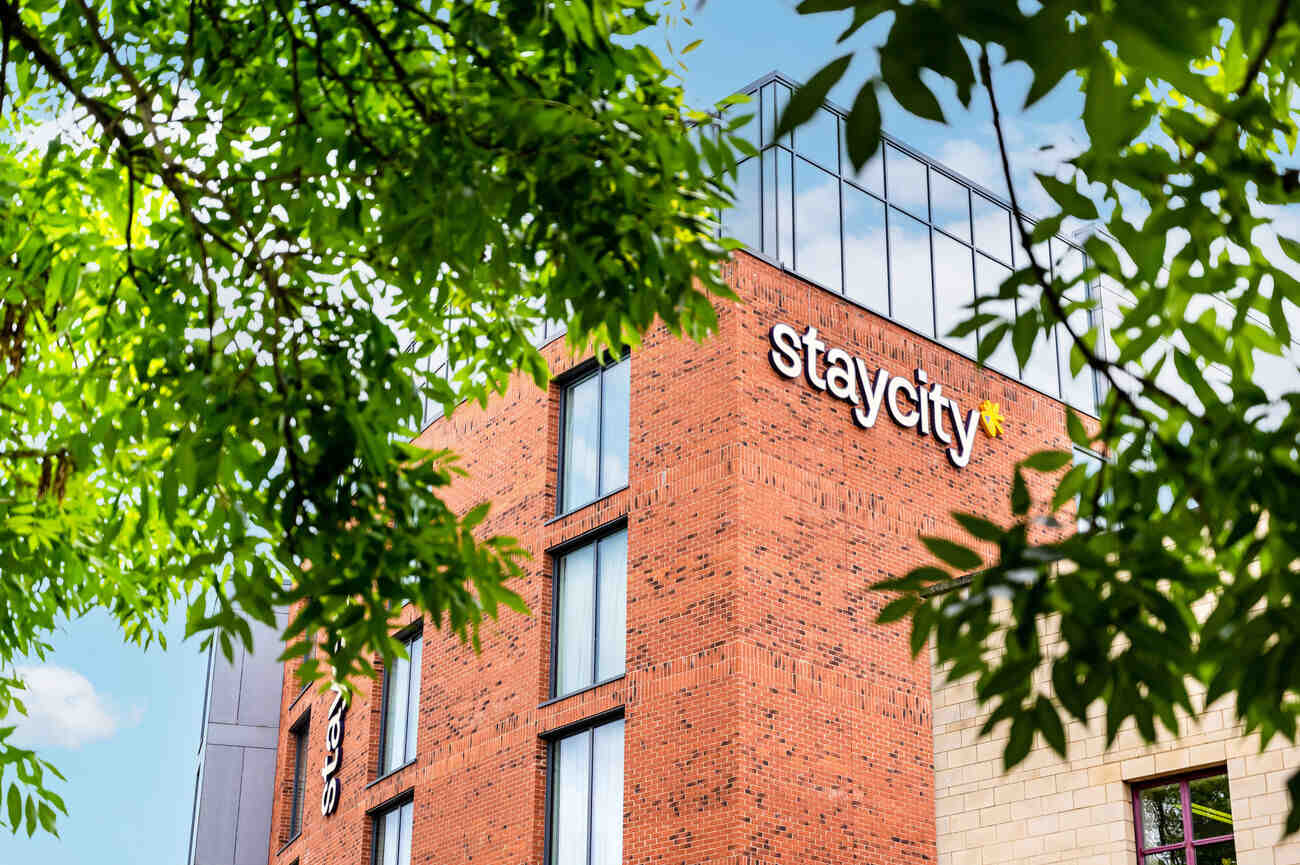 Red brick building with "staycity" sign, surrounded by green leaves and a blue sky.