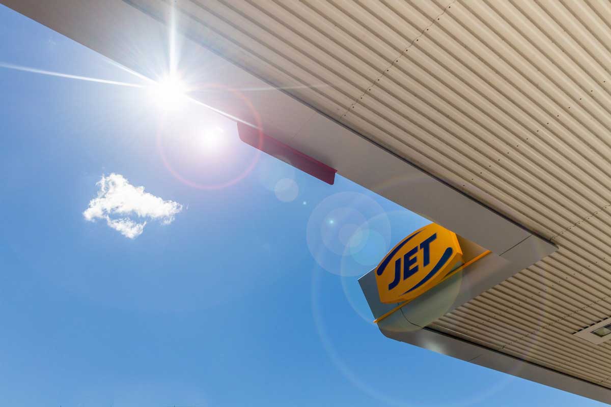 Sun shining above a gas station canopy with a "JET" sign and a small cloud.