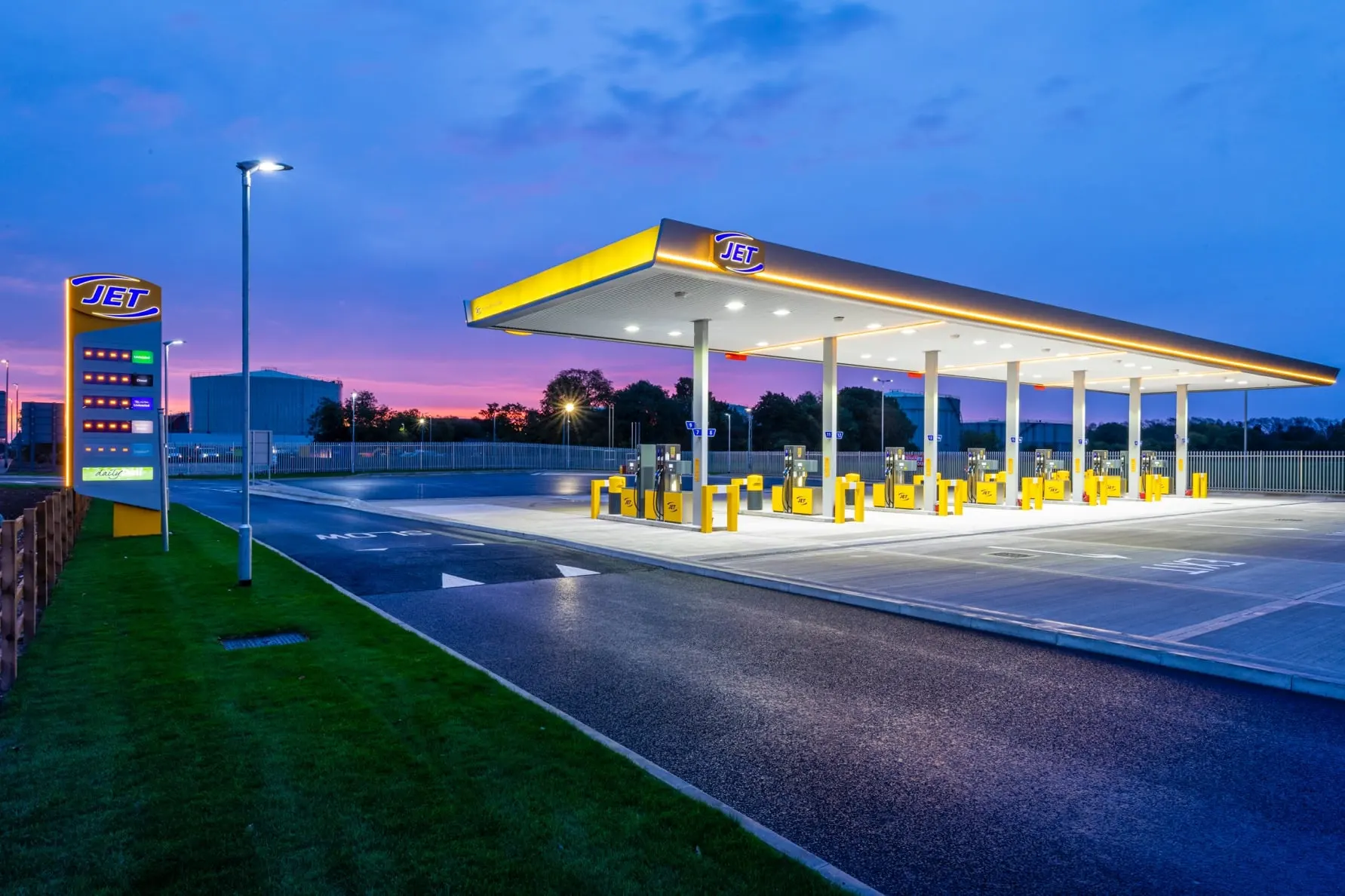 A brightly lit gas station with multiple pumps under a canopy at dusk.