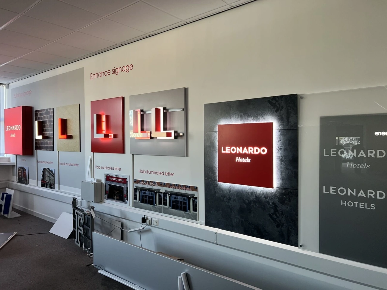 A wall displays various illuminated and non-illuminated "Leonardo Hotels" signage samples in a showroom.