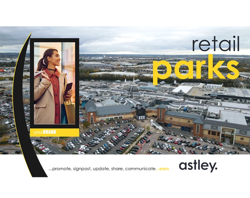 Retail parks aerial view with shopping complex, crowded parking lot, and overcast sky. Foreground features a billboard showcasing a stylish woman holding a smartphone, branded with "your BRAND." Prominent text reads "retail parks" in bold, yellow font. Slogan below: "...promote, sign
