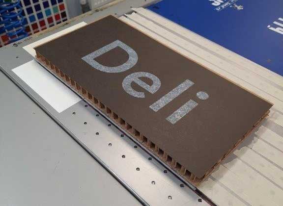 A brown rectangular sign with the word "Deli" in large silver letters.