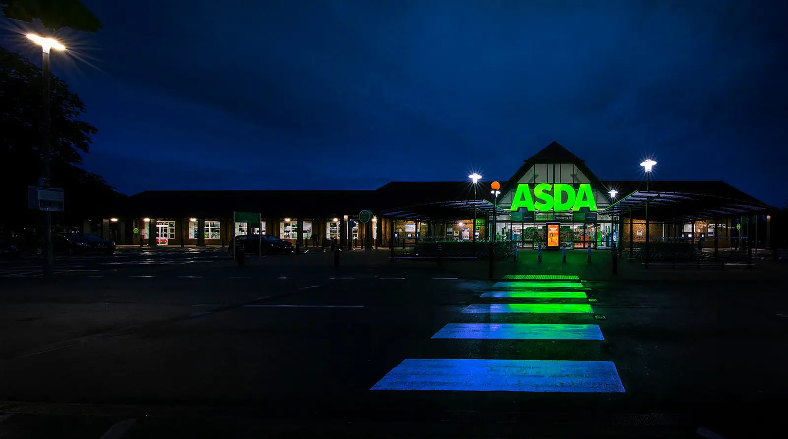 ASDA store at night with illuminated green sign and glowing crosswalk in the foreground.