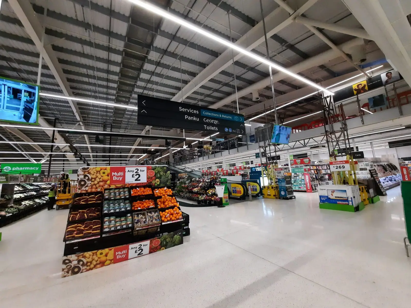 Inside a supermarket with produce displays, overhead signs, and bright lighting.