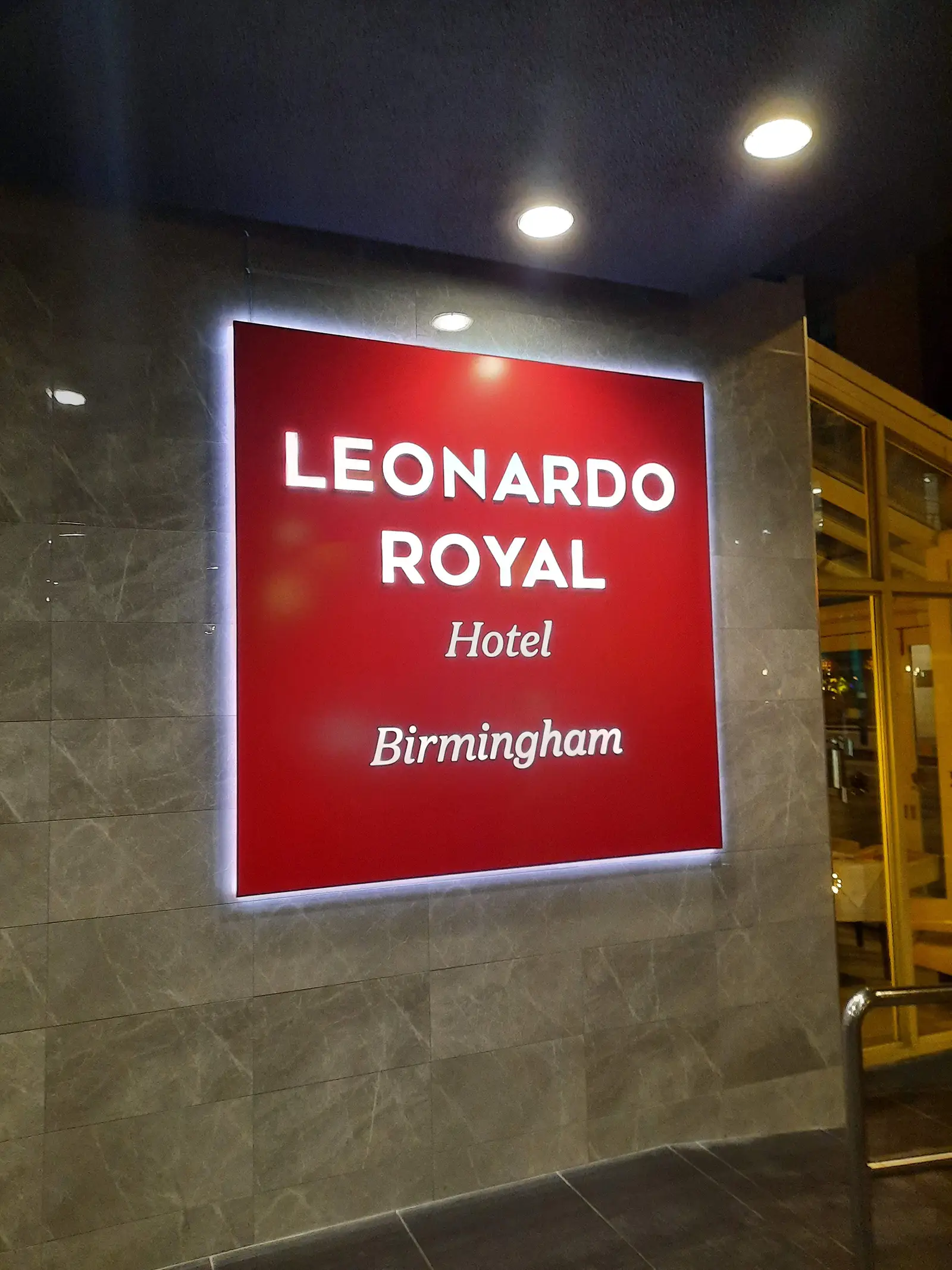 Illuminated red sign for Leonardo Royal Hotel Birmingham on a tiled wall.