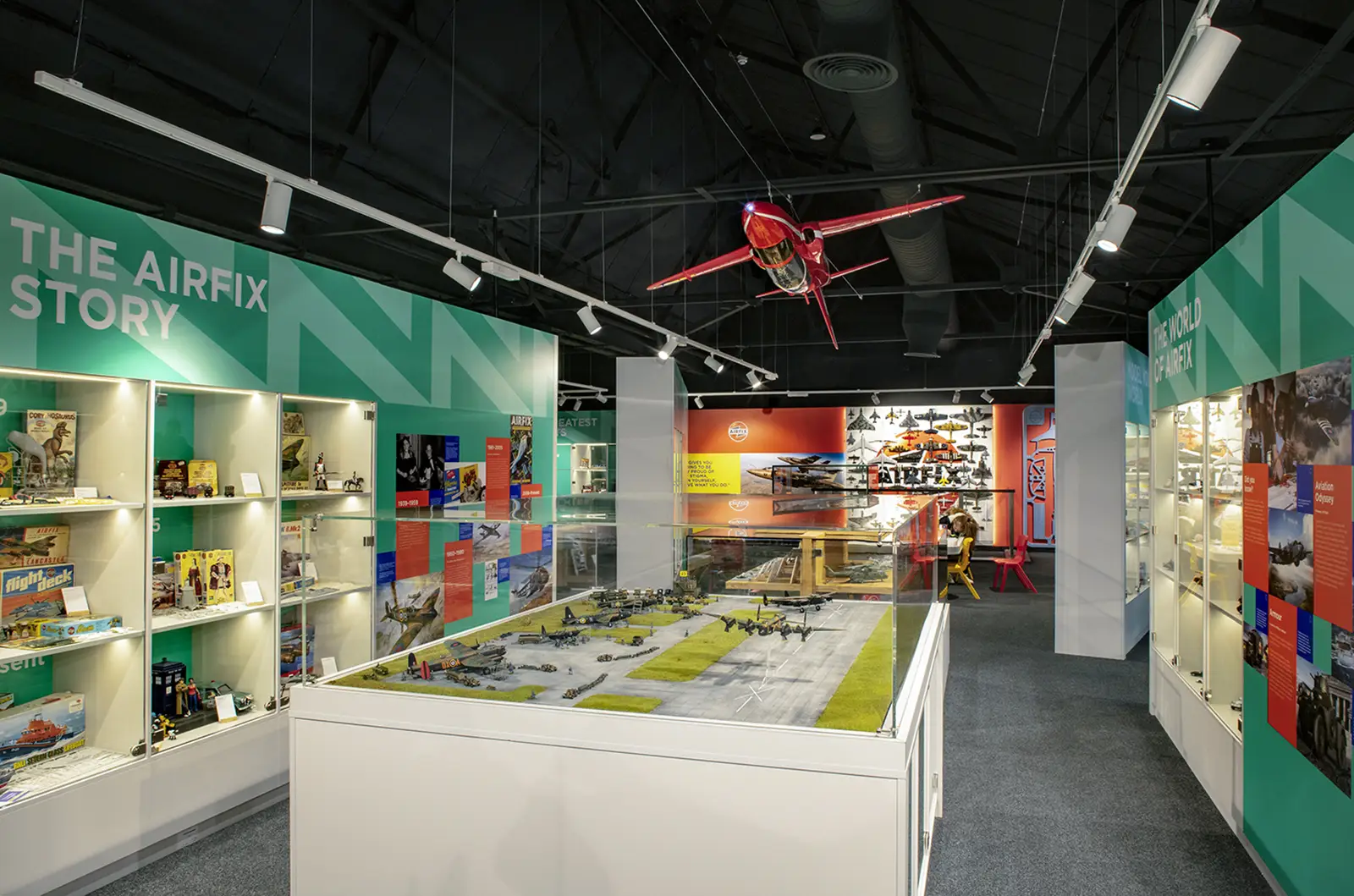 A museum exhibit features model airplanes, display cases, and a suspended red aircraft.