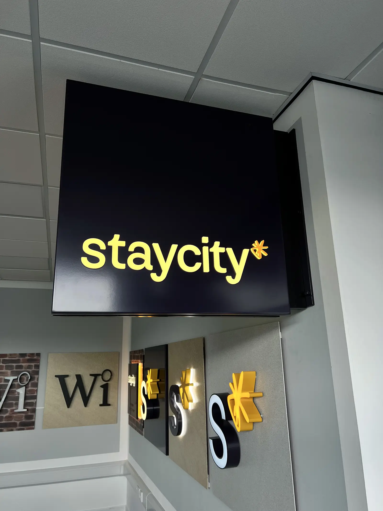 Black sign with yellow text "staycity*" and mirrored reflections on the wall below.