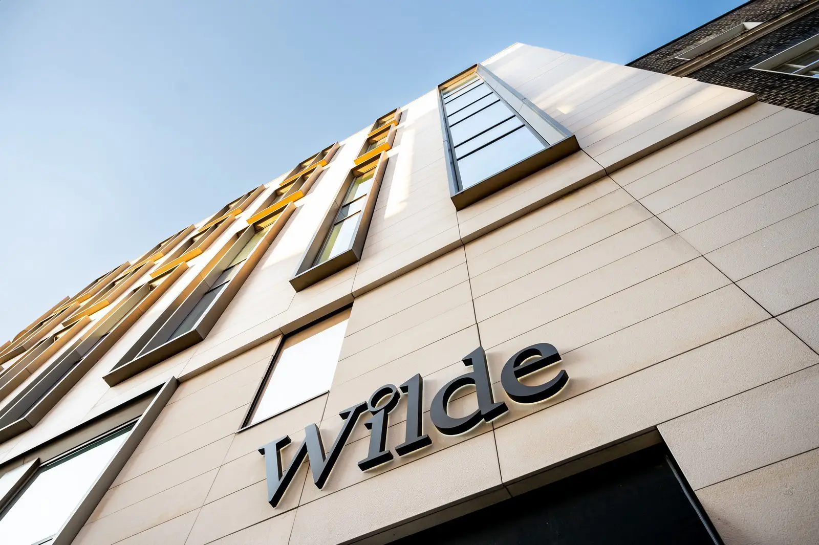 Low-angle view of a modern building facade with "Wilde" sign and large windows.