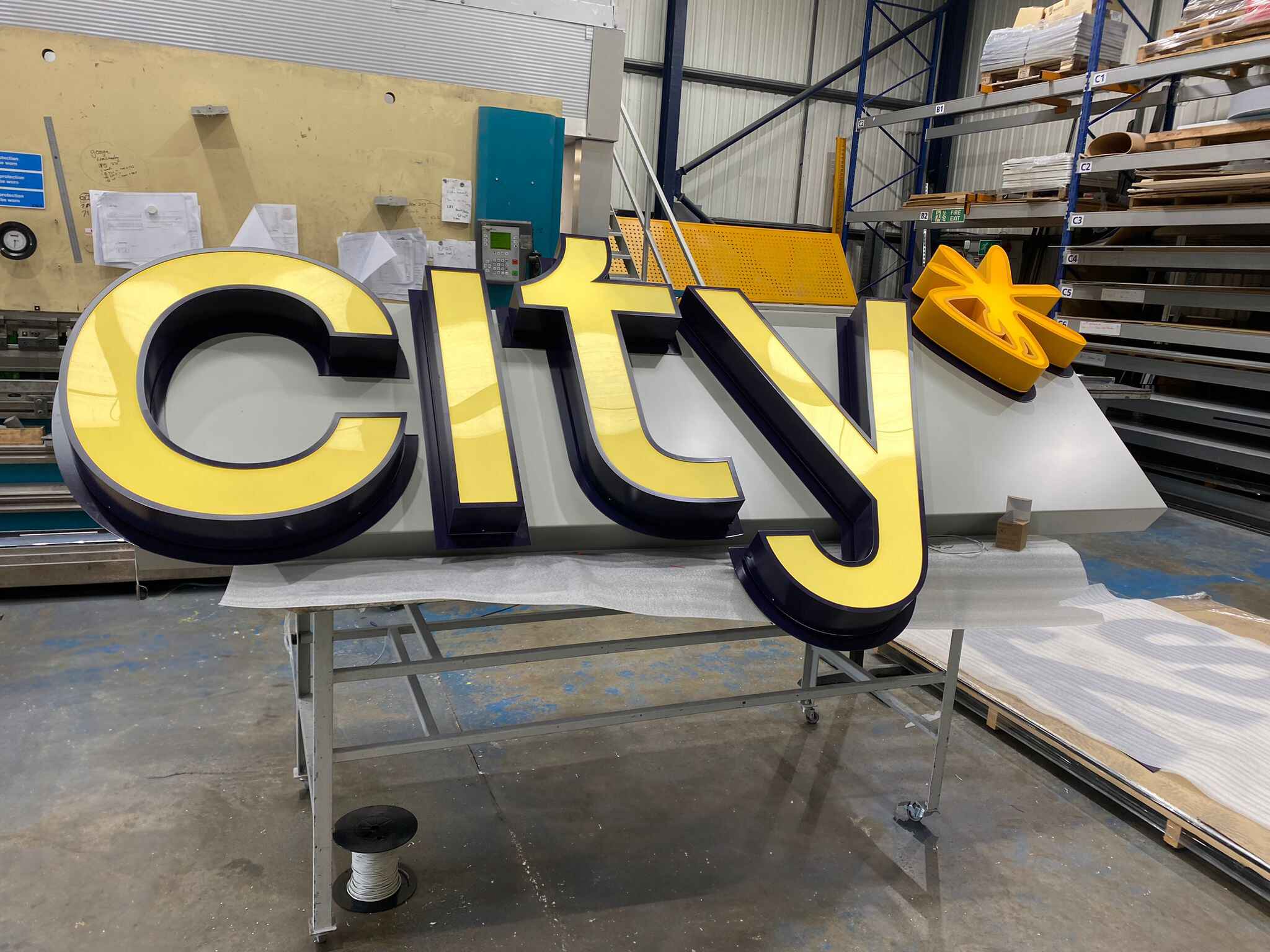 Large yellow and black "city" sign with a starburst symbol on a workshop table.