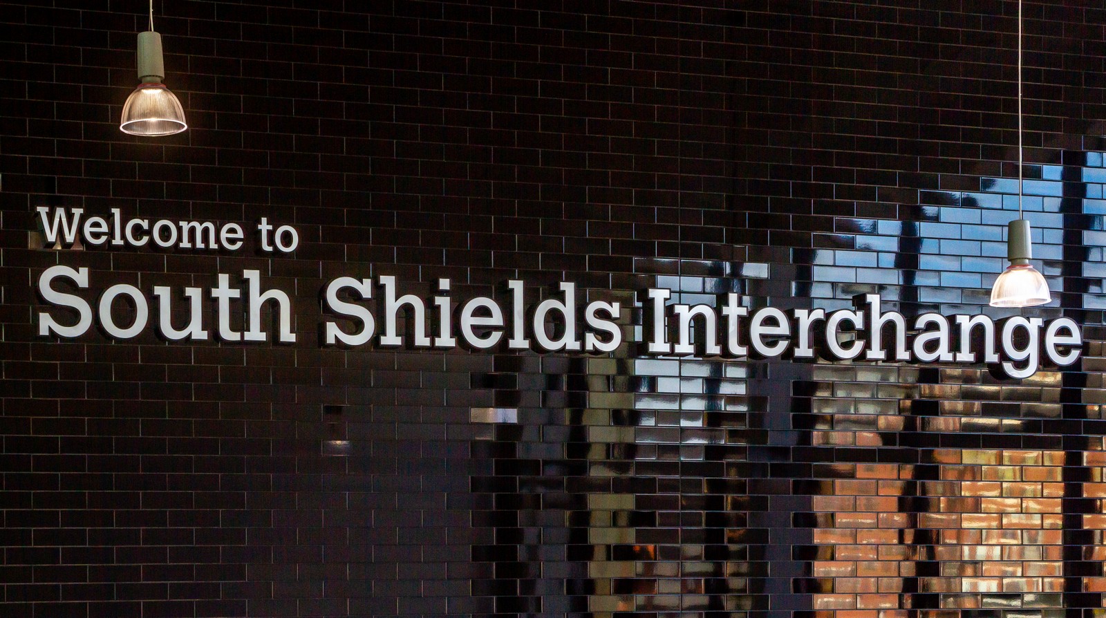 Welcome to South Shields Interchange" sign on a dark tiled wall with hanging lights.
