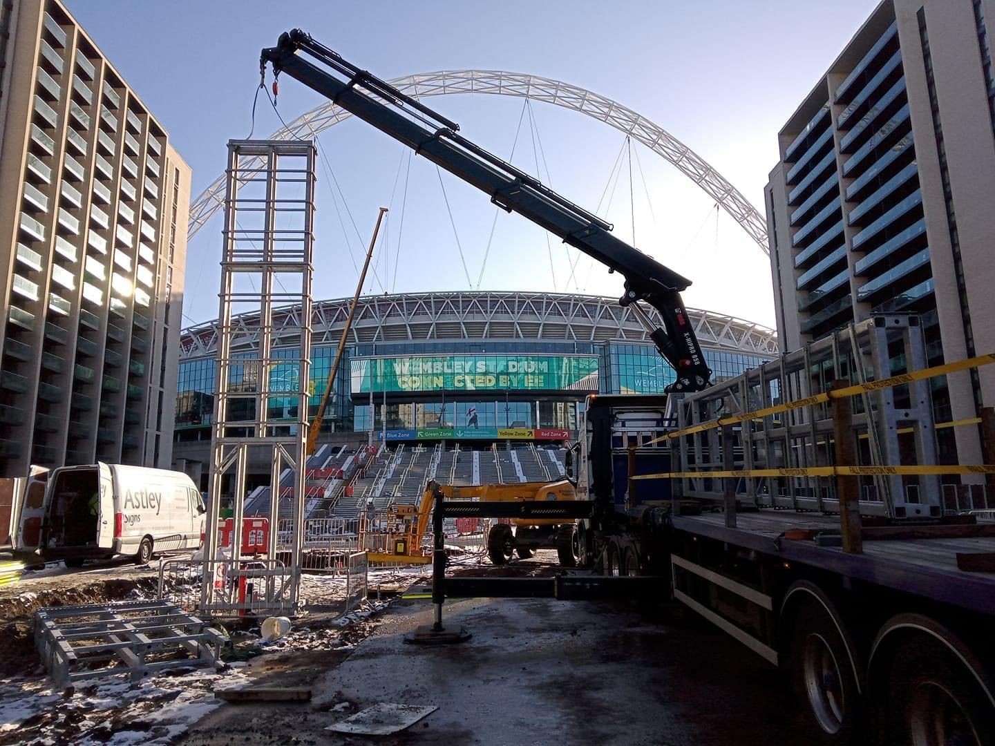 Construction site with a crane and scaffolding in front of a large stadium.
