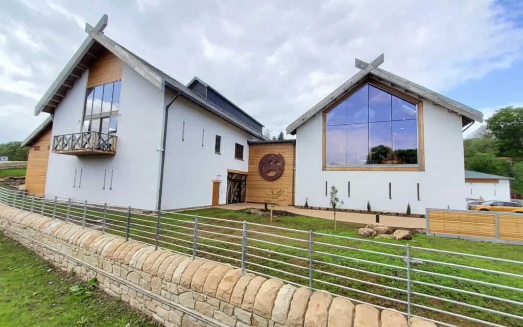 Modern white building with large windows, wooden accents, and a stone wall in the foreground.