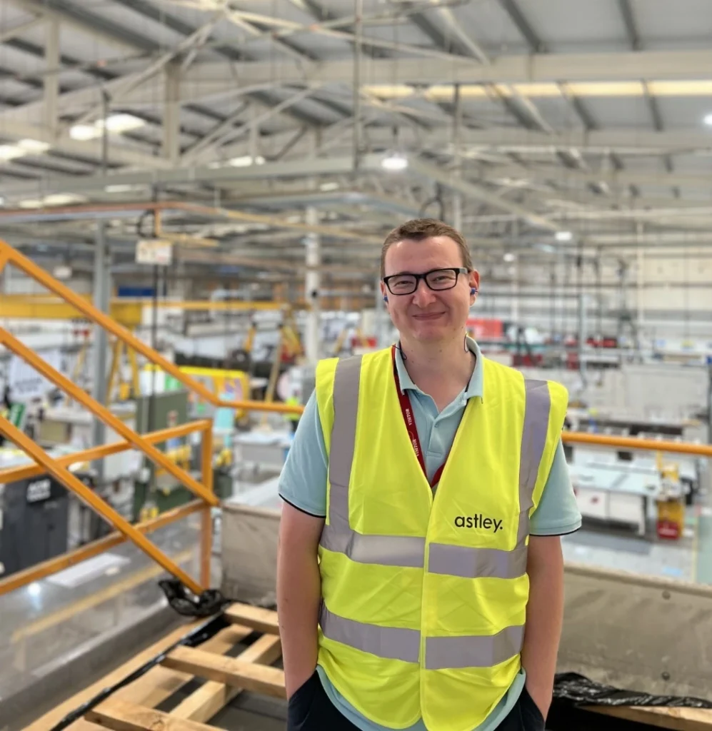 A person wearing a yellow safety vest stands in an industrial warehouse with machinery.