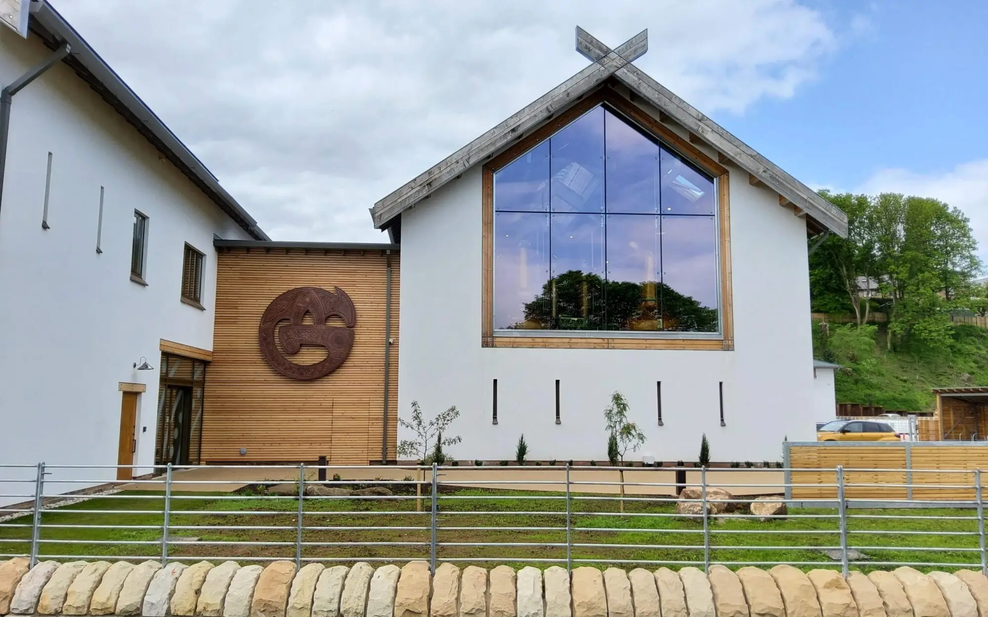 Modern building with large glass windows, wooden accents, and a circular wall sculpture.