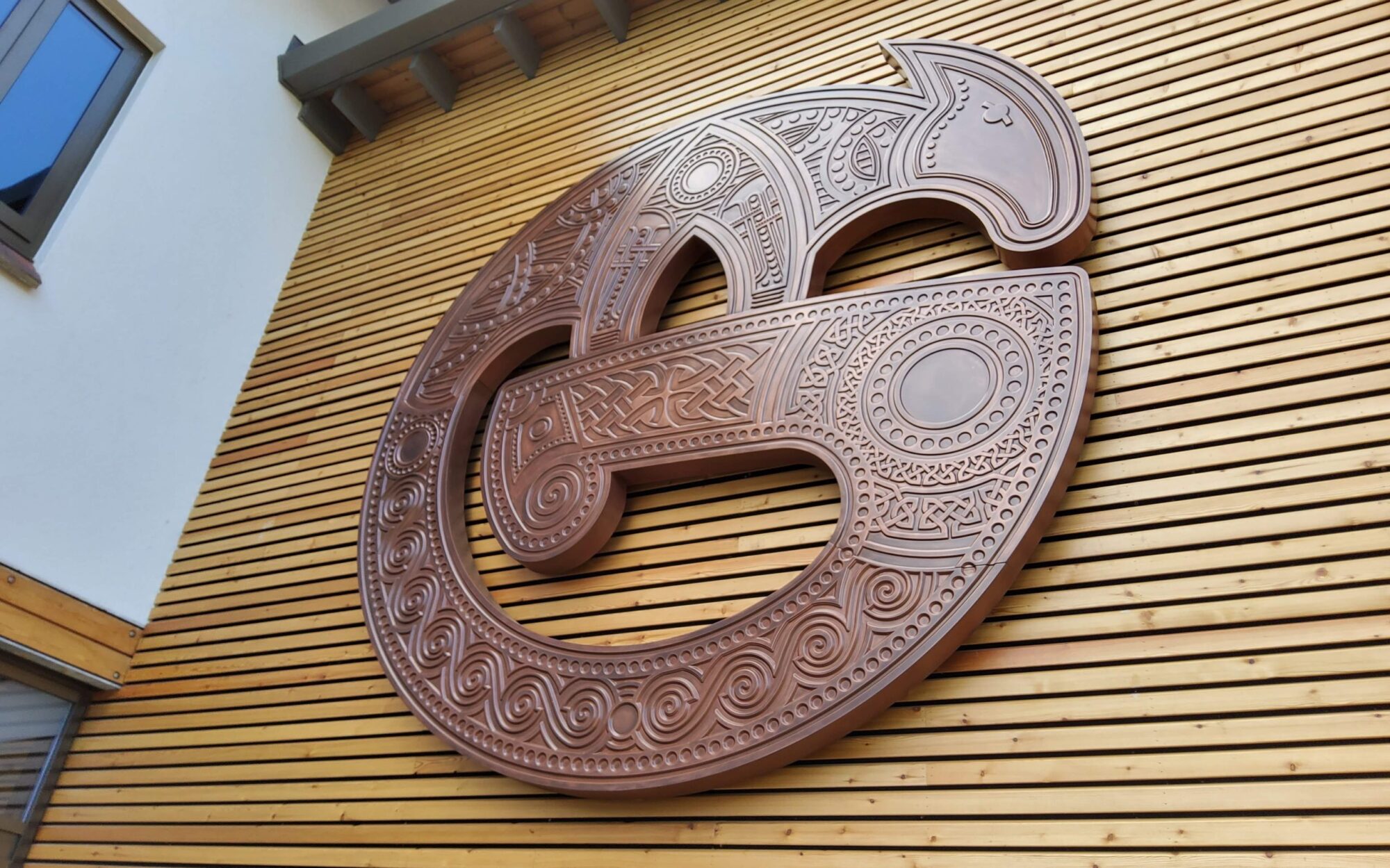 Large, intricately carved wooden sculpture mounted on a wooden slatted wall.