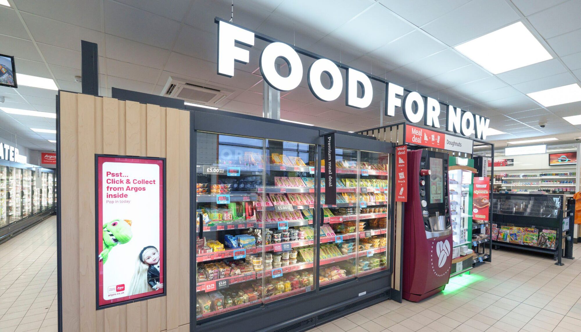 Supermarket aisle with a "Food for Now" sign, refrigerated section, and a digital kiosk.
