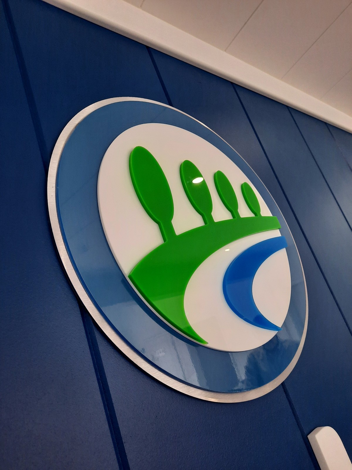 A circular logo with green spoons and a blue curve on a blue wall.