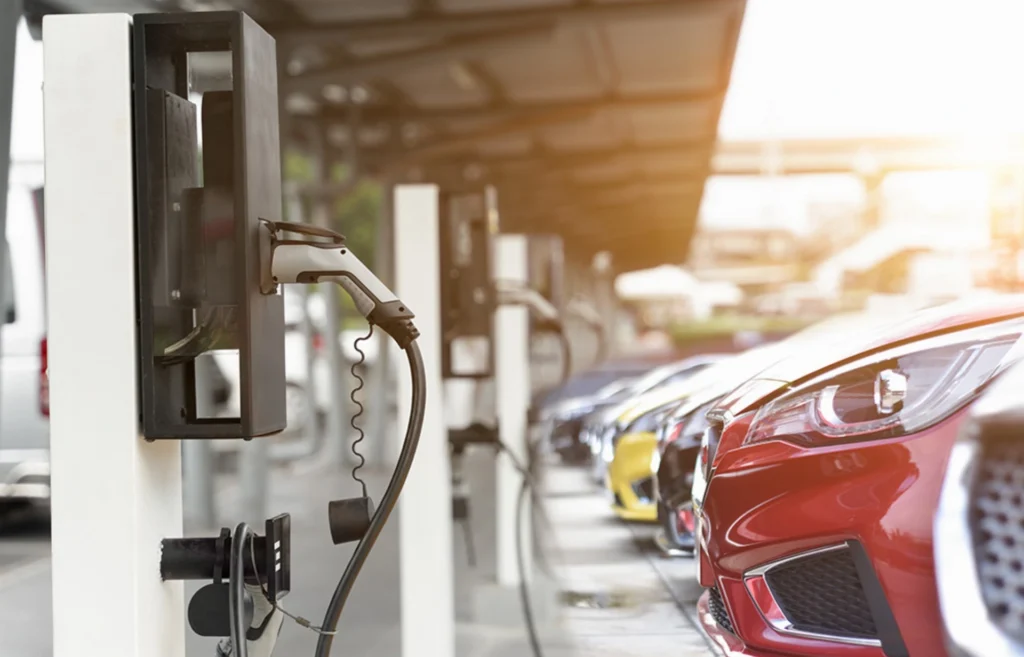 Electric cars parked in a row, each connected to a charging station under a canopy.
