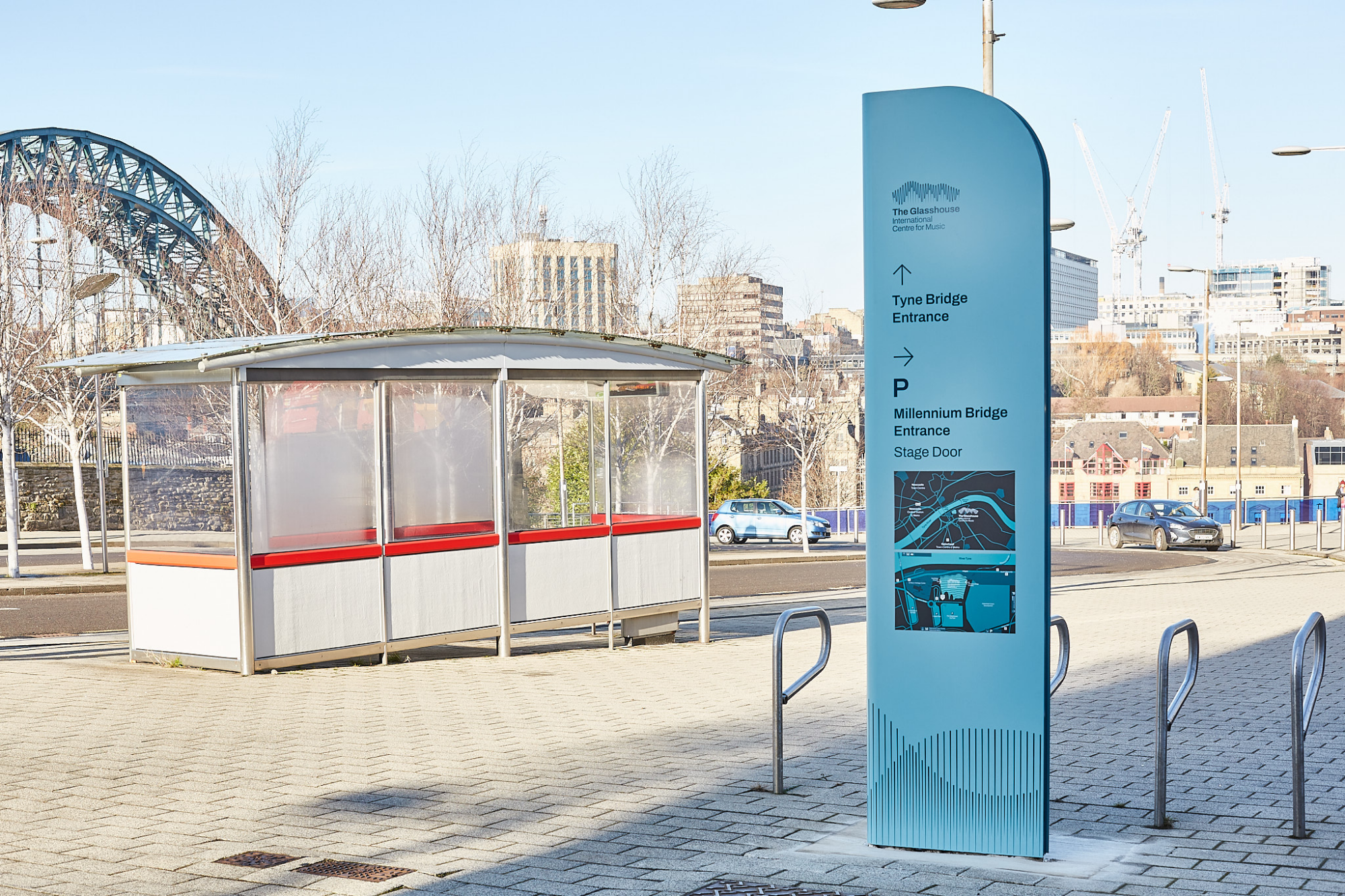 A blue information sign and a bus shelter are near a bridge in an urban area.