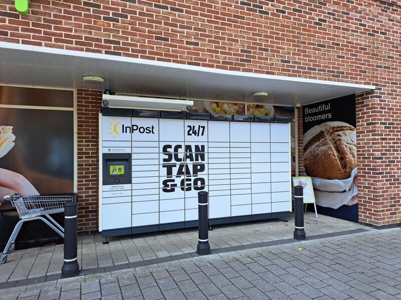 Outdoor InPost locker with "Scan Tap & Go" sign, next to a shopping cart and bread poster.