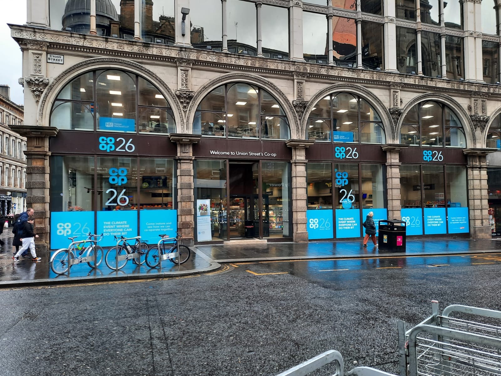 A Co-op store with large arched windows and blue signage on a rainy street.