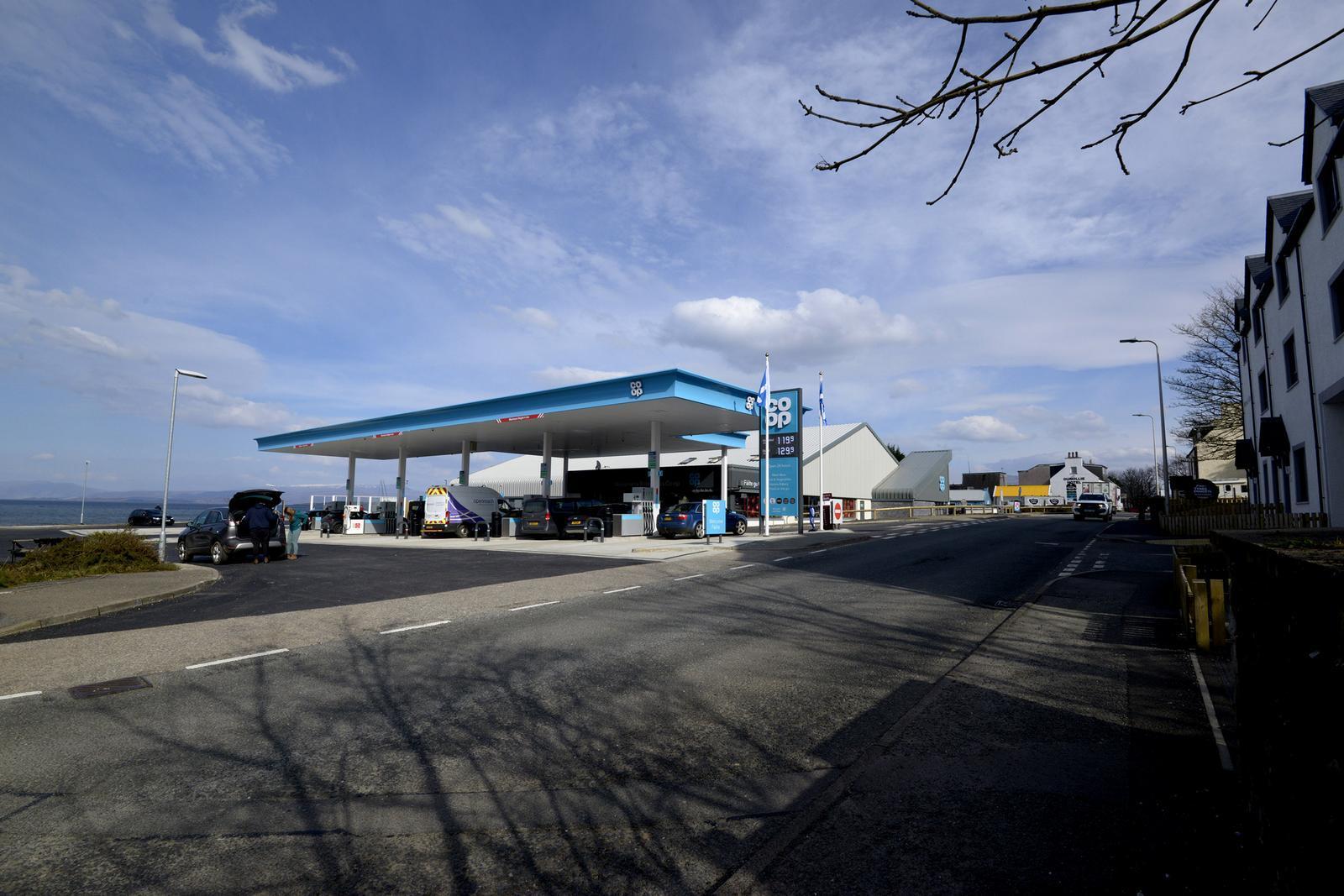 A gas station with a blue roof is situated beside a quiet road under a cloudy sky.