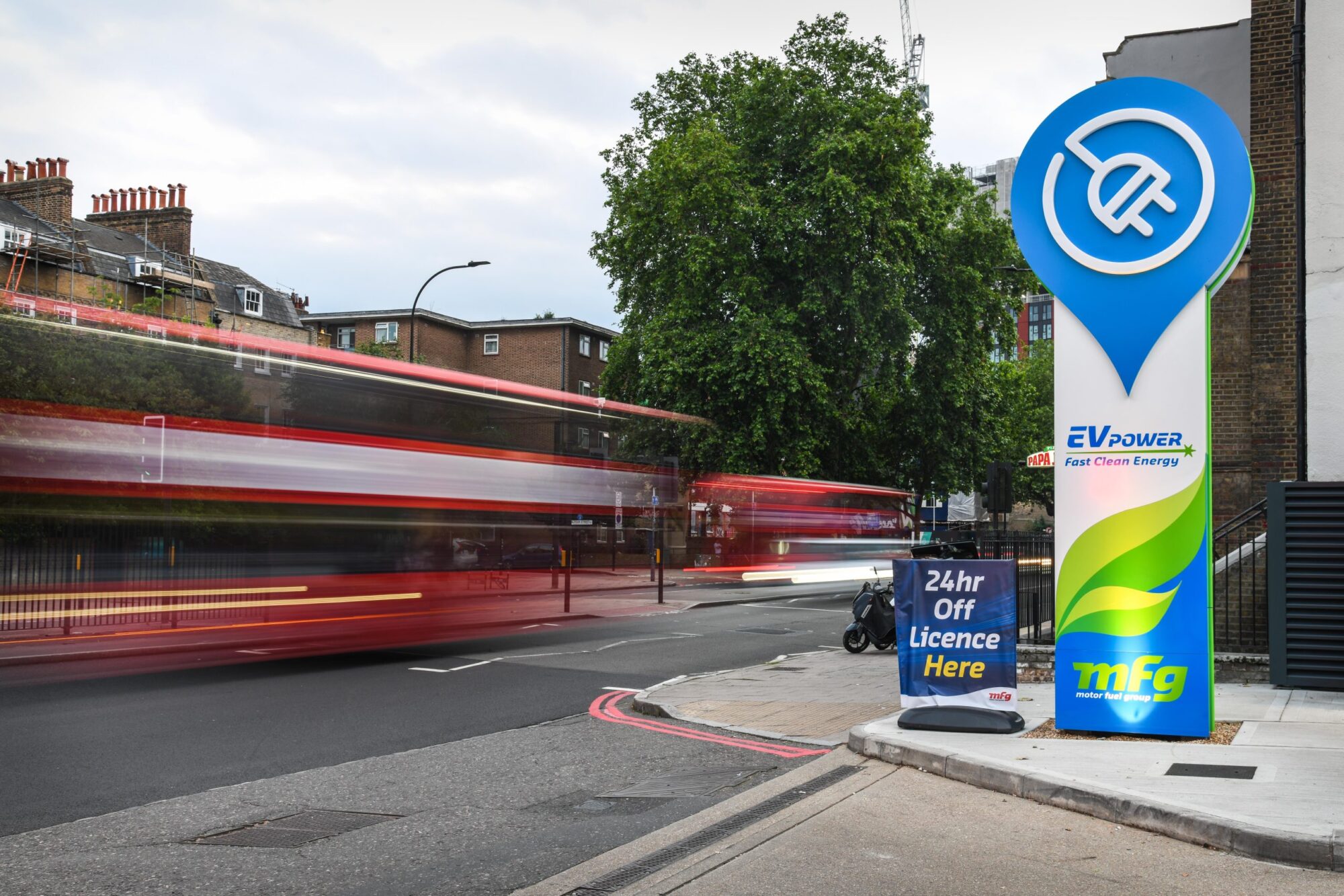 A blurred red bus passes an EV charging station on a city street.
