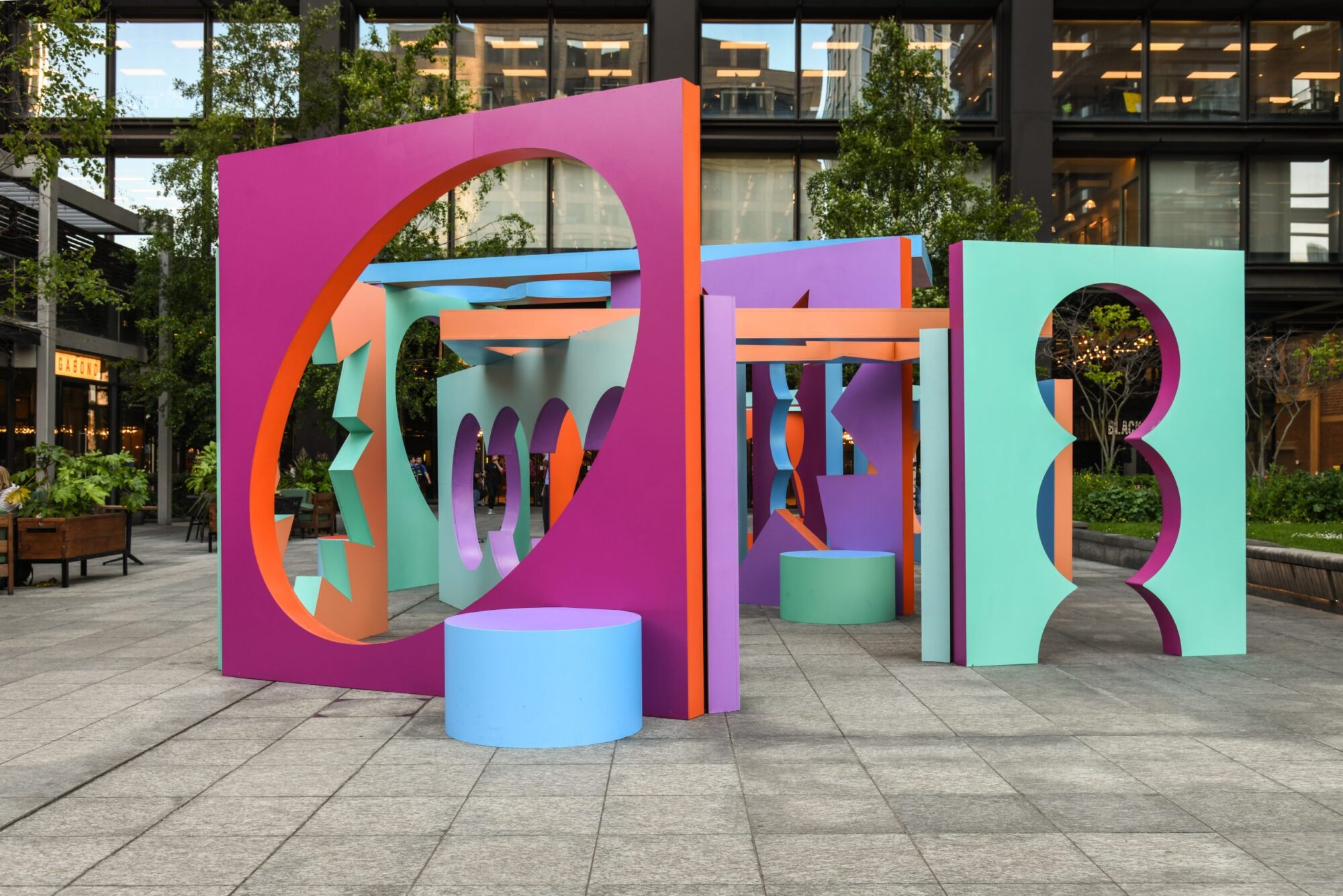 Colorful geometric sculptures with circular cutouts stand on a paved area near a modern building.