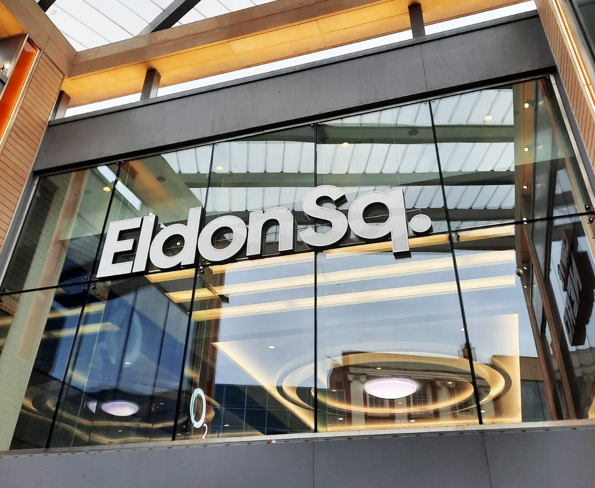 Glass facade of Eldon Square with large white letters and reflections of interior lights.