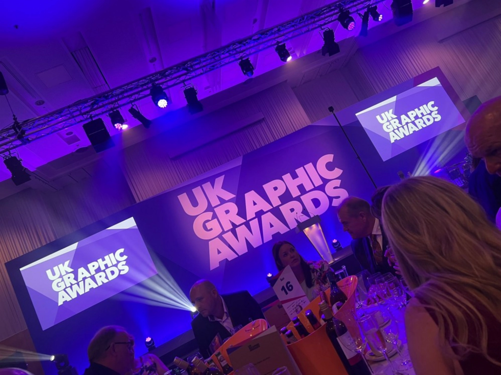 People seated at tables under purple lighting at the UK Graphic Awards event.