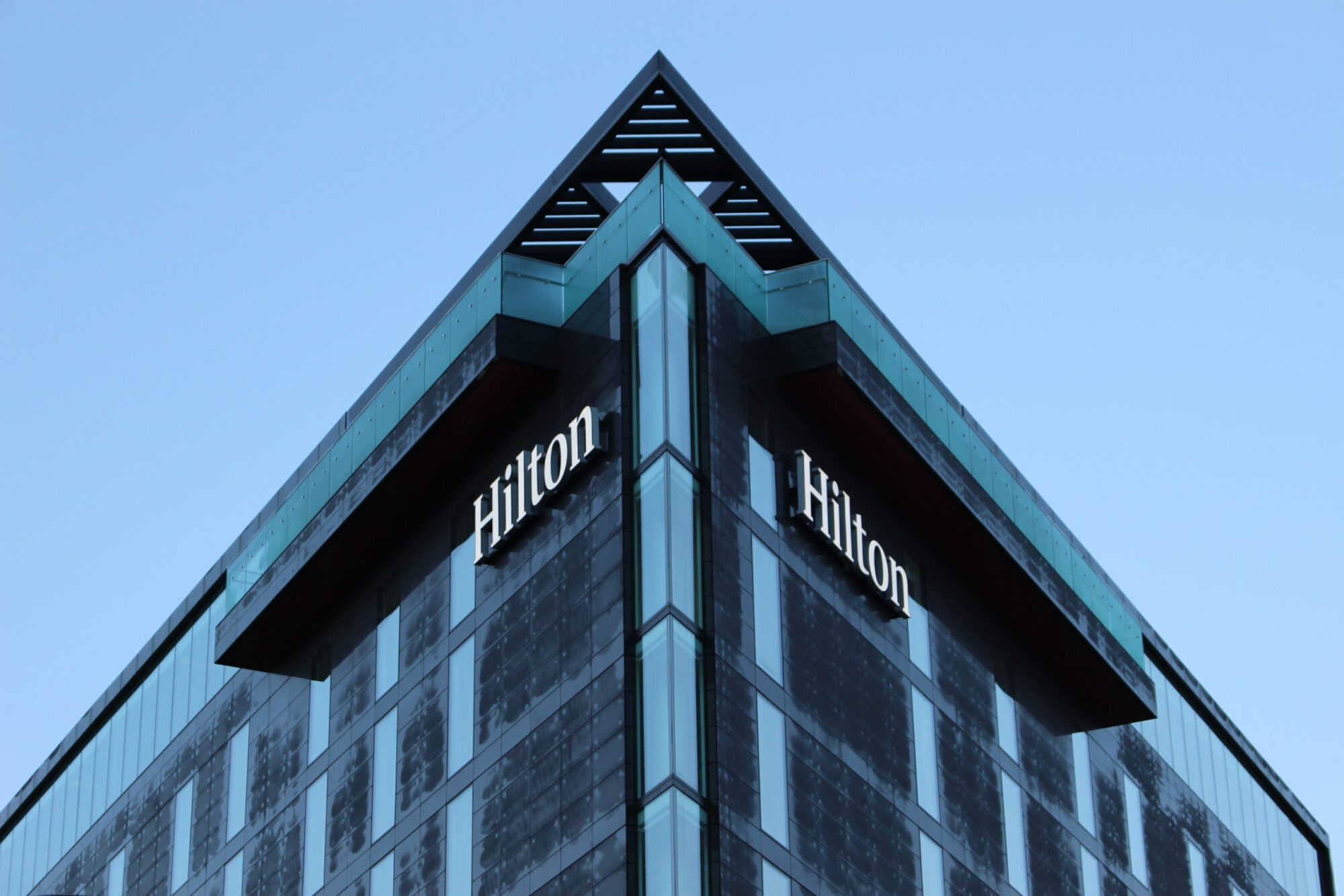 The corner of a modern building with "Hilton" signs against a clear blue sky.