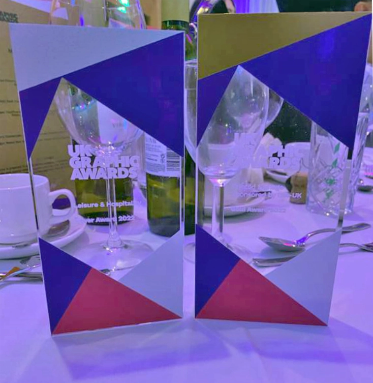 Two geometric-patterned awards on a table with wine glasses and a menu in the background.