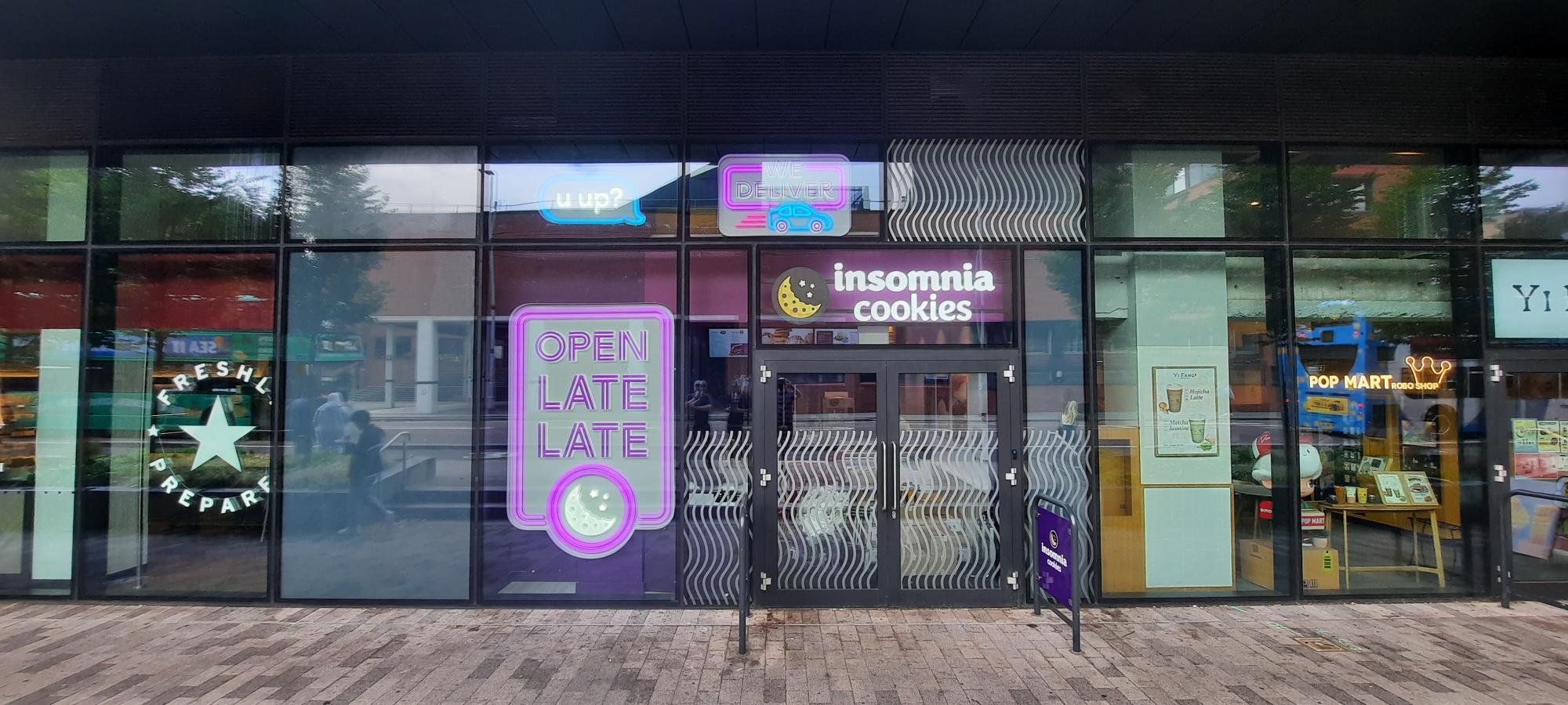Storefront with "Insomnia Cookies" sign, neon "Open Late" sign, and various colorful window displays.