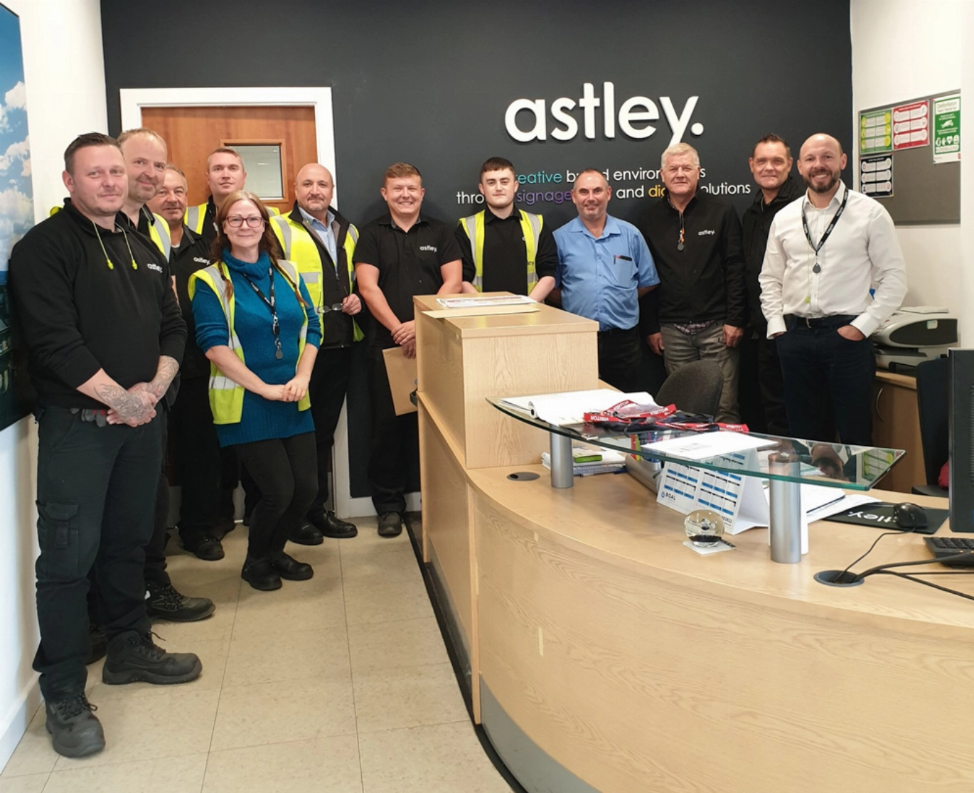 A group of eleven people standing in an office with a curved reception desk.
