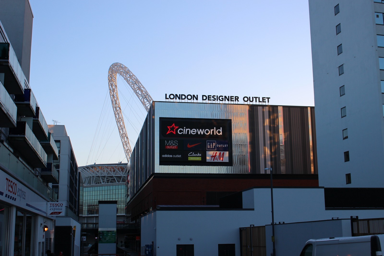 London Designer Outlet building with Cineworld sign, surrounded by tall structures and Wembley Stadium arch.