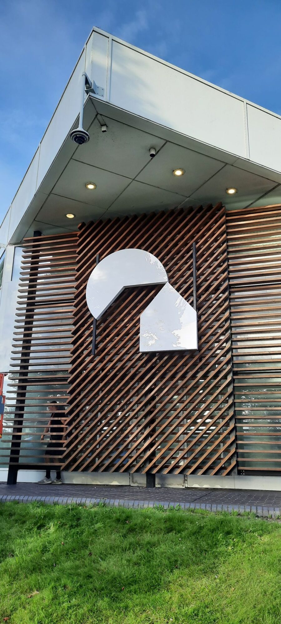 Modern building facade with wooden slats and a large, abstract white logo.