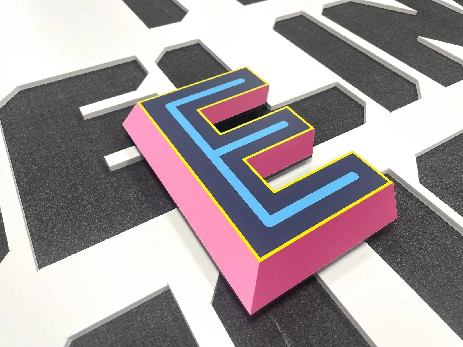 A 3D letter "E" with pink sides and blue top outlined in yellow.