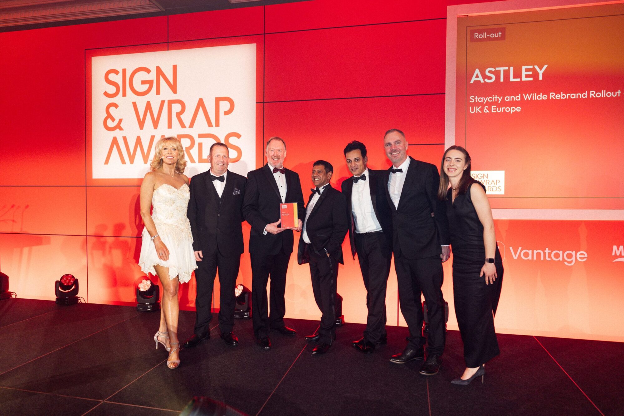 Seven people in formal attire stand on stage at the Sign & Wrap Awards event.