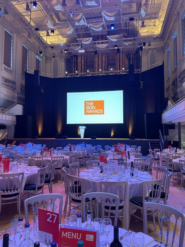 Elegant banquet hall with round tables, chairs, and a stage displaying "The Sign Awards.