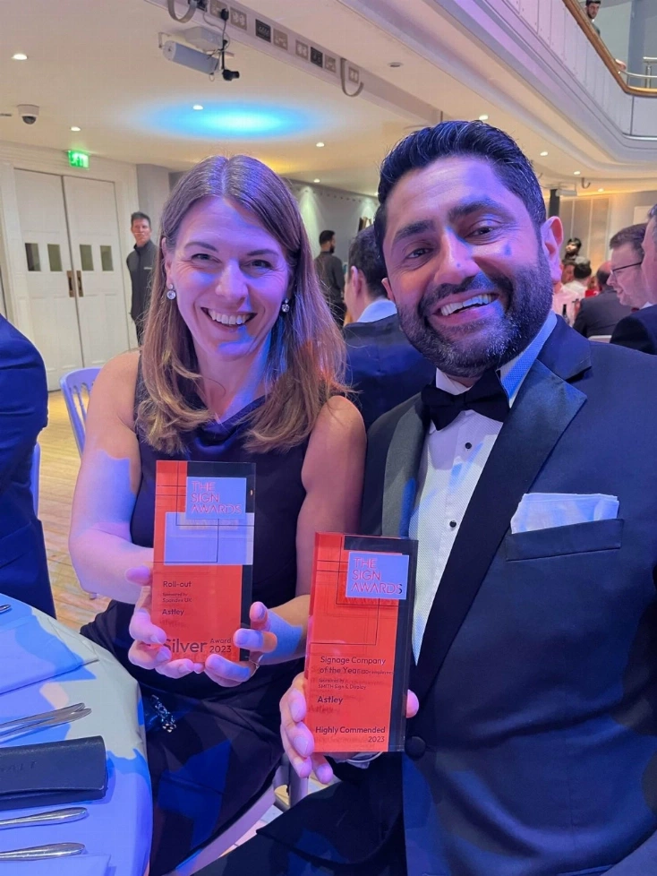 Two people in formal attire smiling and holding awards at a banquet event.