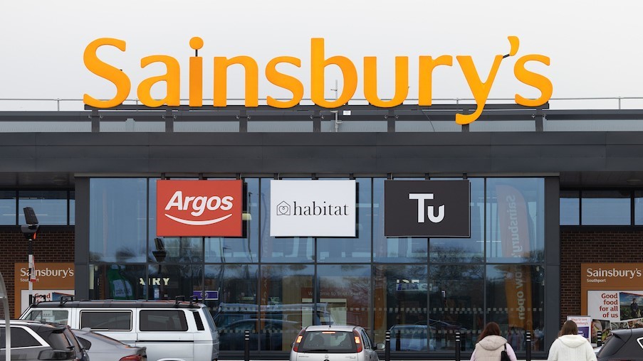 Sainsbury's storefront with Argos, Habitat, and Tu signs above parked cars.