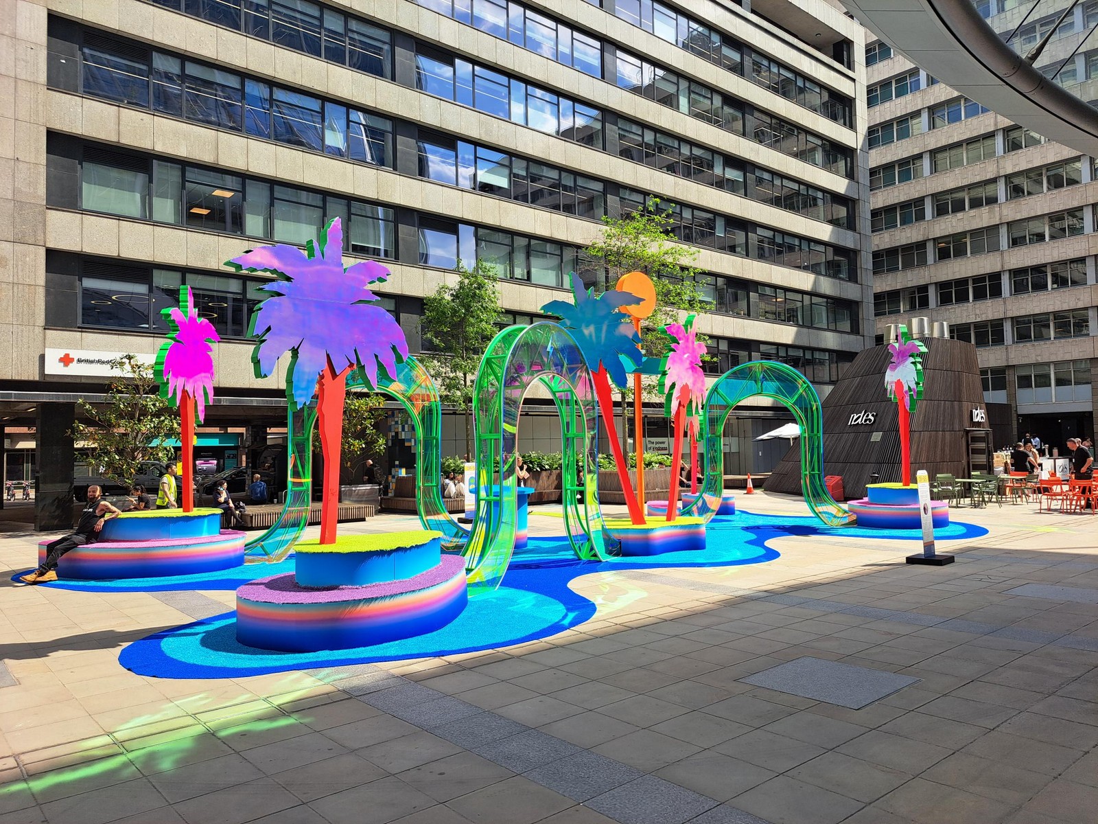 Colorful palm tree sculptures and arches in a courtyard surrounded by modern buildings.