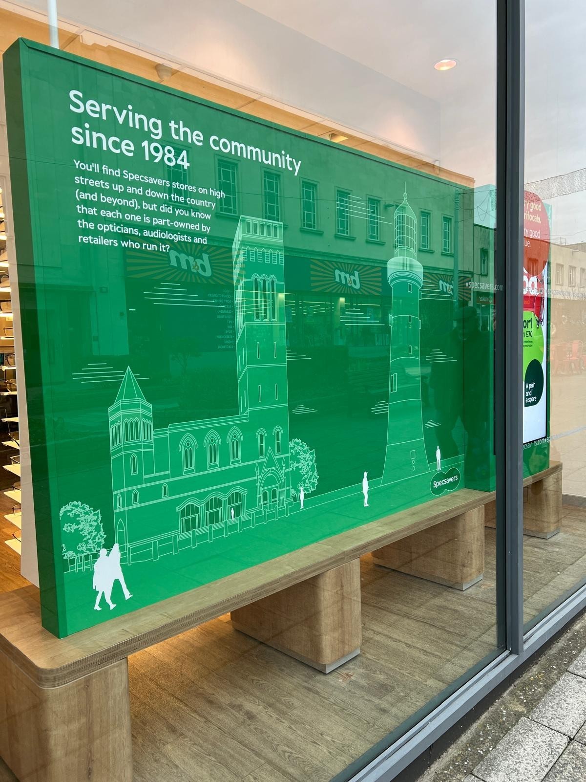 Large green sign in a store window with white text and building illustrations.