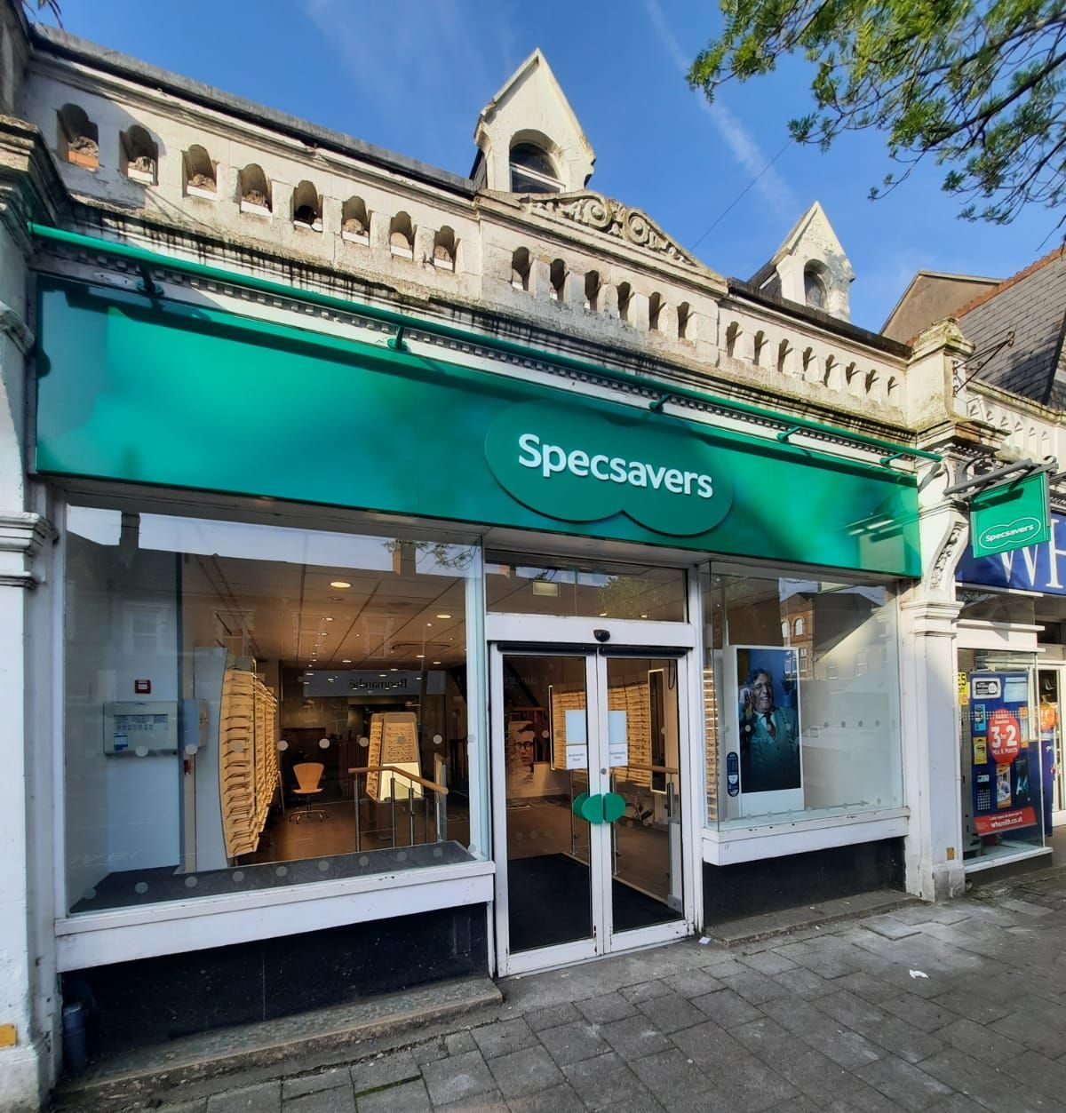A Specsavers store with a green sign and glass doors on a sunny day.