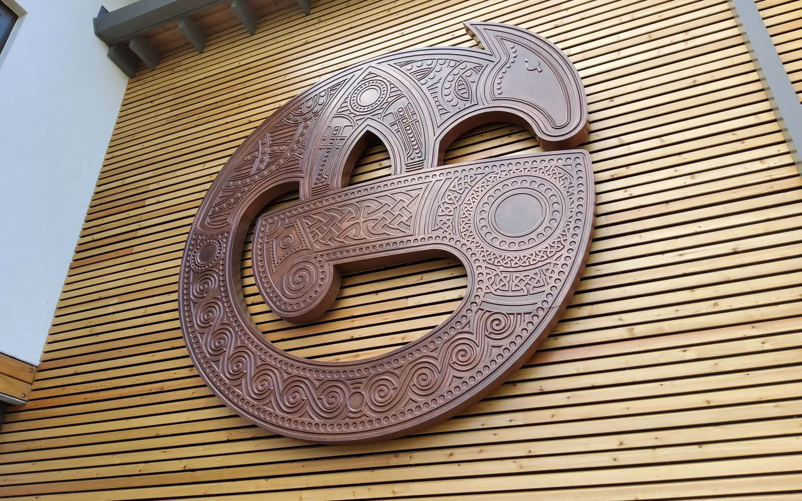 Large, intricately carved wooden sculpture mounted on a wall with horizontal wooden slats.