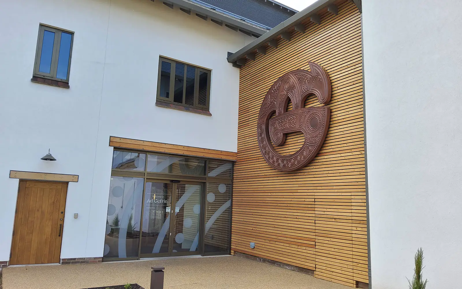 Modern building with wooden accents, large circular wooden sculpture, and glass entrance door.