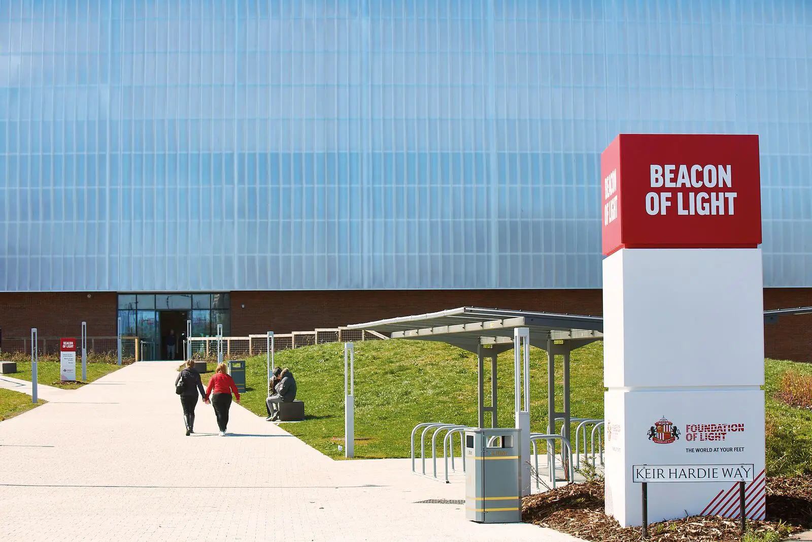 Two people walk towards a large building with a sign reading "Beacon of Light.