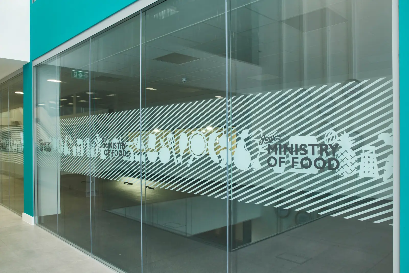 Glass wall with diagonal stripes and "Ministry of Food" text in a modern interior.