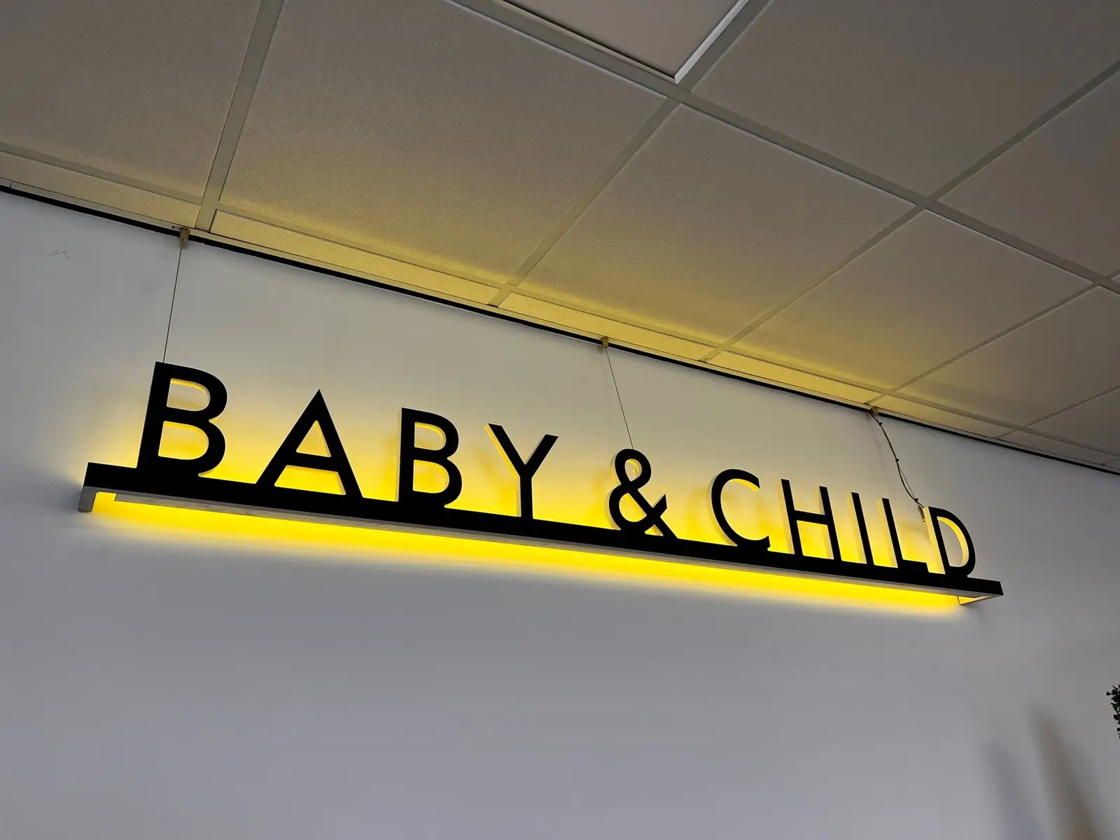 A black "BABY & CHILD" sign with yellow backlighting hangs from a white ceiling.